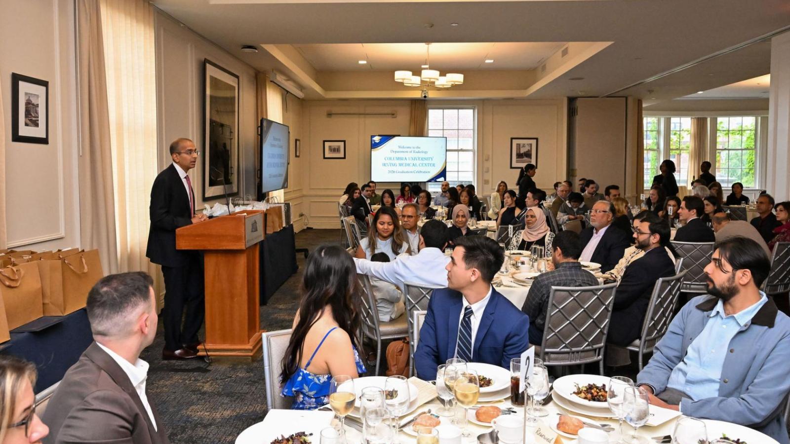 Man at podium talks to room of seated people