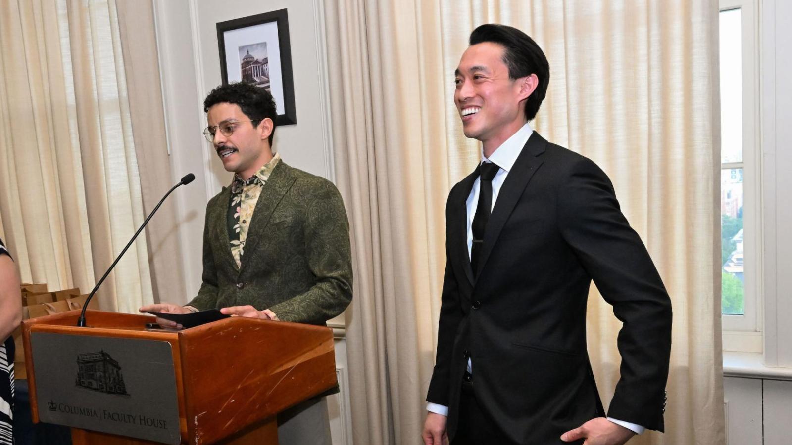 Man at podium next to smiling man in suit